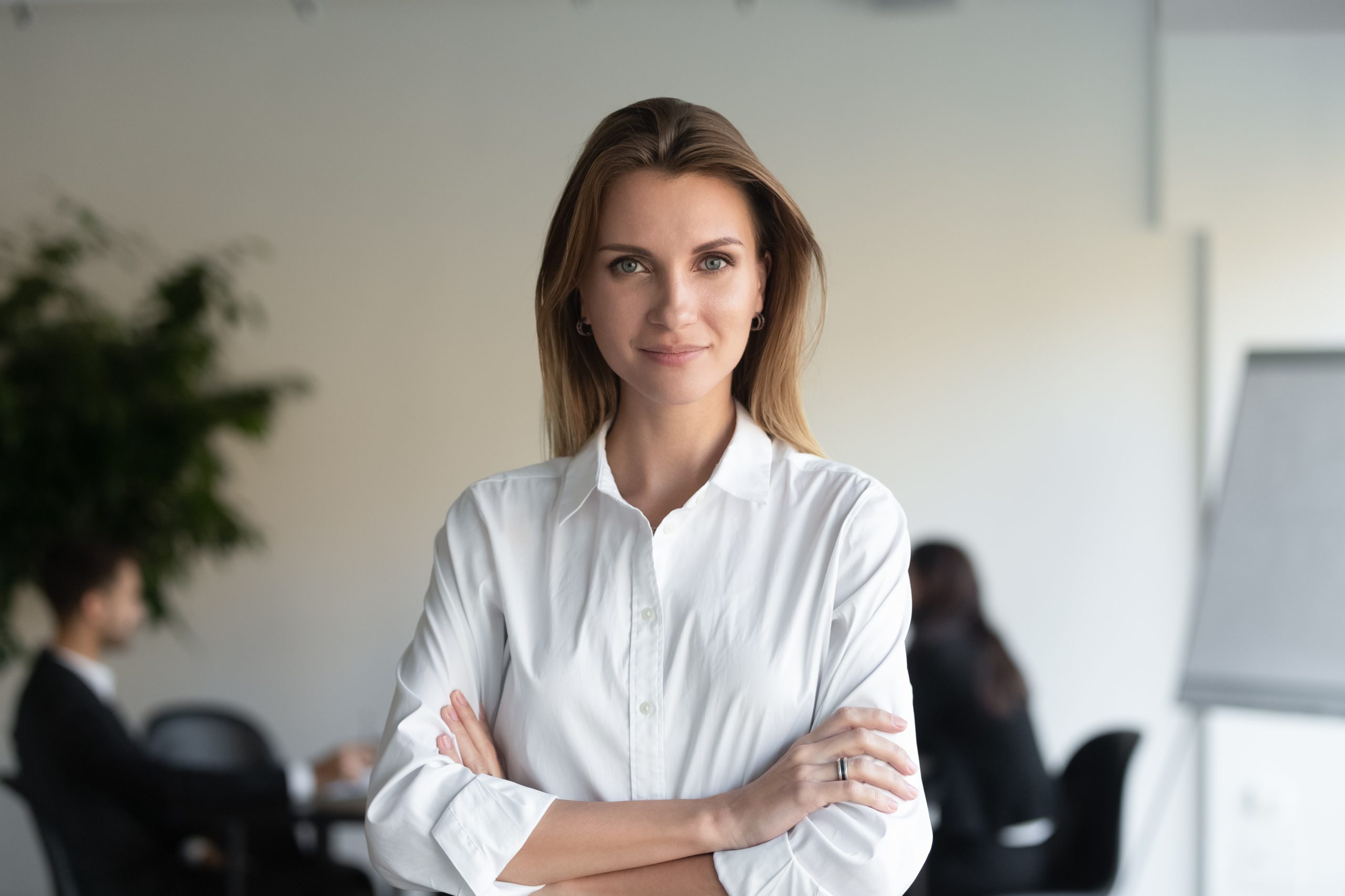 Headshot portrait of confident young businesswoman stand forefront with arms crossed looking at camera, successful millennial female ceo or boss posing for picture in office, leadership concept